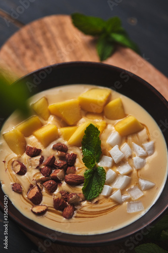 Tropical smoothie bowl with banana, mango, coconut and nuts. Refreshing dessert with mint on an old wooden table. Diet and delicious breakfast for the whole family.
