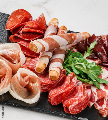 Antipasto platter cold meat with grissini bread sticks, prosciutto, slices ham, beef jerky, salami on slate stone board over marble background. Meat appetizer