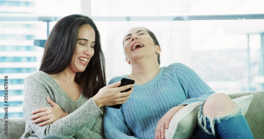 Two women having fun with phone while sitting on sofa Two women having fun with phone while sitting on sofa