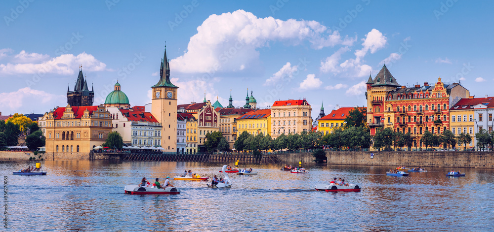 Fototapeta premium Scenic embankment in Prague city with paddle boats on Vltava river and Charles bridge; Historical center of Prague, buildings and landmarks of old town, Prague, Czech Republic