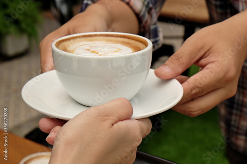 Close-up woman hand taking coffee cup from Waitress between sitting in cafe , hand giving cup of coffee to someone that sitting at coffee shop while working outside office