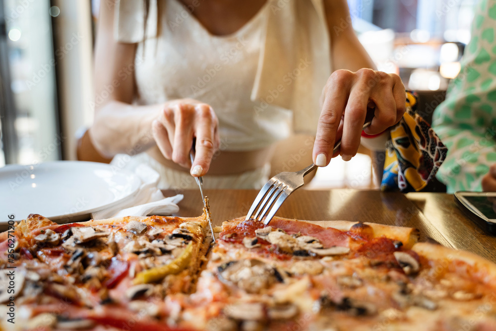 Close up on slice of pizza unknown caucasian woman slicing food from the plate at the restaurant in summer day front view unhealthy eating