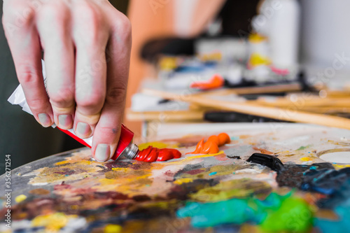 the artist squeezes red oil paint onto the palette