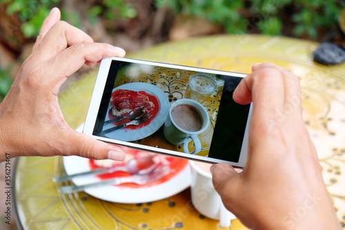 Woman's hand holding blank screen mobile phone during eat sweet cake  in cafe, female using  and reading cellphone between  breaking and relaxing time in coffee shop