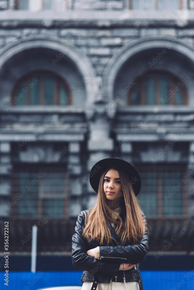 Attractive female standing with crossed arms on the street, glamorous hipster girl looking at you