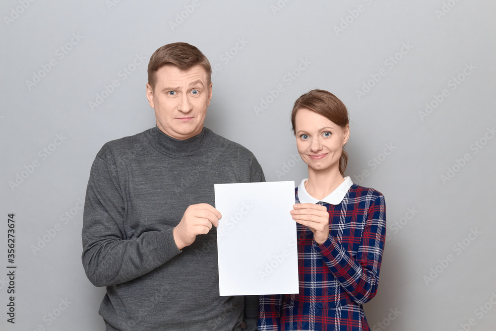 Portrait of adult couple holding together white blank paper sheet Portrait of adult couple holding together white blank paper sheet