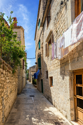 Fototapeta Naklejka Na Ścianę i Meble -  Narrow street in historic town Trogir, Croatia. Travel destination. Narrow old street in Trogir city, Croatia. The alleys of the old town of Trogir are very picturesque and full of charm. Croatia.