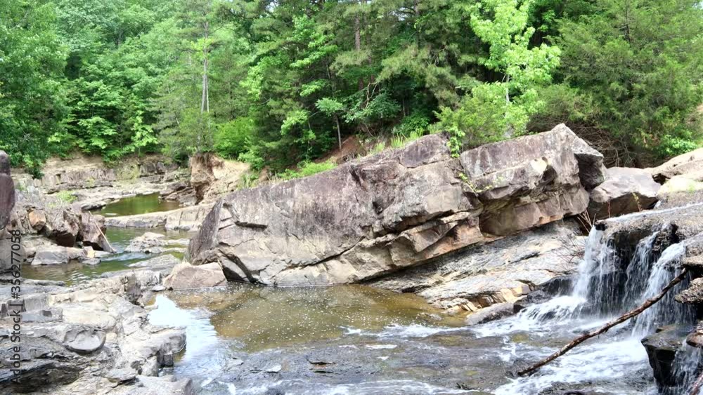 A mountain valley waterfall flows into a creek among the trees and rocky ledges A mountain valley waterfall flows into a creek among the trees and rocky ledges