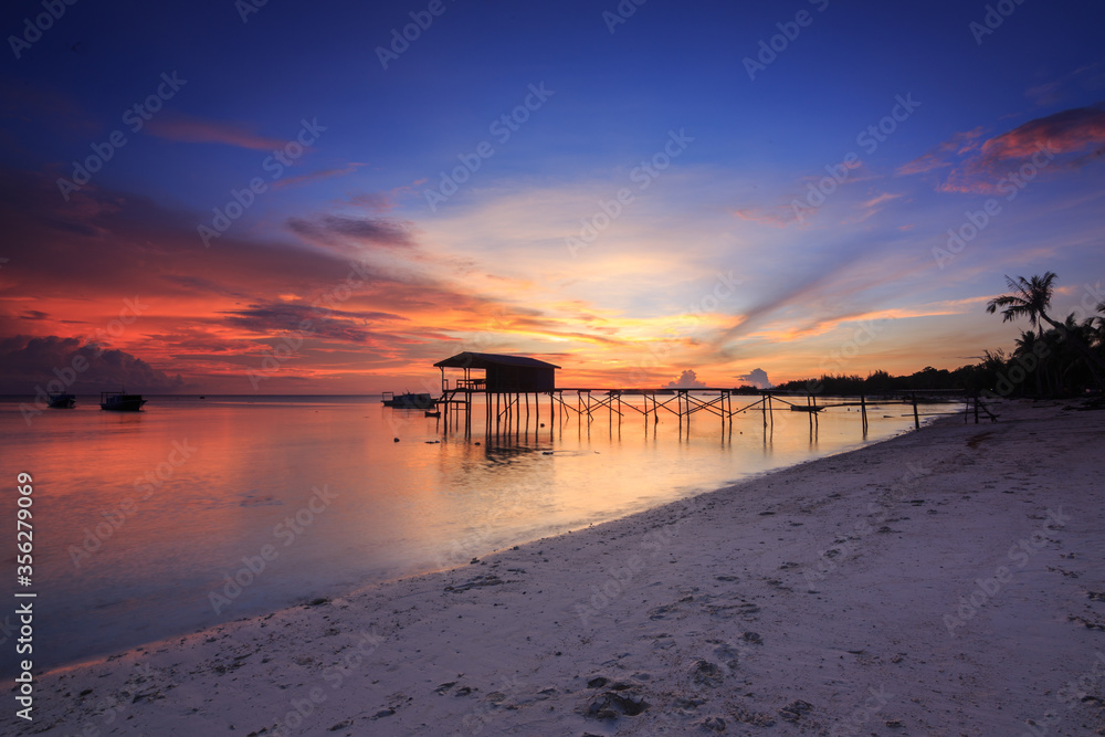 Amazing beautiful sunset with silhouette wooden jetty and coconut tree