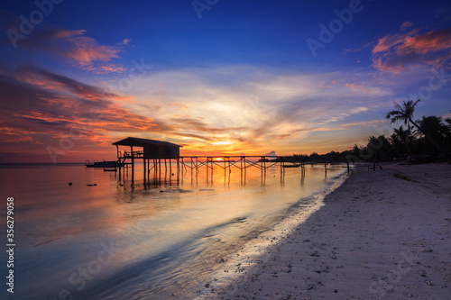 Amazing beautiful sunset with silhouette wooden jetty and coconut tree