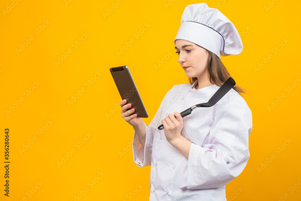 Cooking recipes. Cooking according to recipes. A girl in a chef's uniform looks at new recipes on a tablet. Cuisine of the world. National cooking. Cooking recipes. Cooking according to recipes. A girl in a chef's uniform looks at new recipes on a tablet. Cuisine of the world. National cooking.