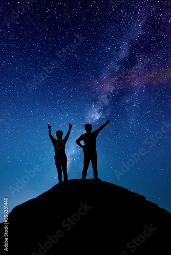 Milky Way with people on the mountain. Landscape with night sky with stars and silhouette of standing happy man and woman who pointing finger in starry sky. Milky way with travelers. Beautiful galaxy © noon@photo