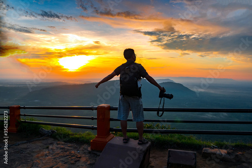 A photographer standing on top of Mountain at sunset with Mist.Asian male backpack in nature during sunset Relax time on holiday concept travel at Pha mor i dang Sisaket province Thailand ASIA.