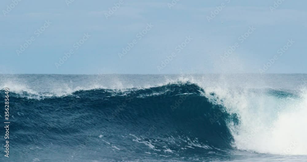 A large wave breaking into an arc into a dark blue sea with large plumes of spray. A large wave breaking into an arc into a dark blue sea with large plumes of spray.