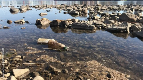 Rocky riverbank. Trash and dirty foam float on the water. River pollution by industrial waste.