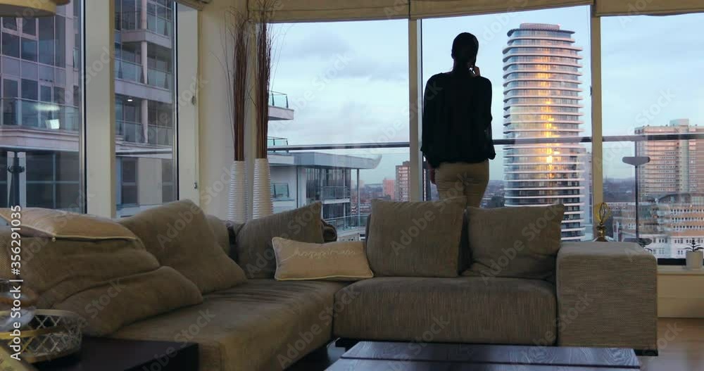 A woman working in a city apartment - A fashionably dressed woman talking on her smartphone in her city apartment A woman working in a city apartment - A fashionably dressed woman talking on her smartphone in her city apartment