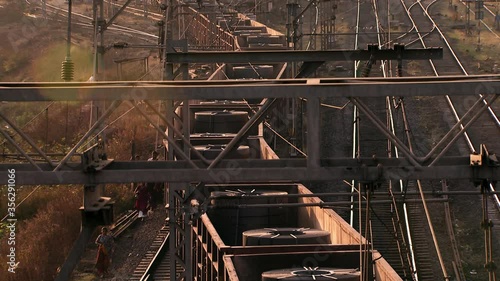 Trains moving slowly along tracks under a network of gantries and pylons, at sunset.  photo