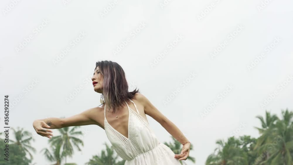 mind and body connection with nature - middle aged attractive and happy Asian Chinese woman in Summer dress enjoying dancing free at idyllic tropical green field mind and body connection with nature - middle aged attractive and happy Asian Chinese woman in Summer dress enjoying dancing free at idyllic tropical green field