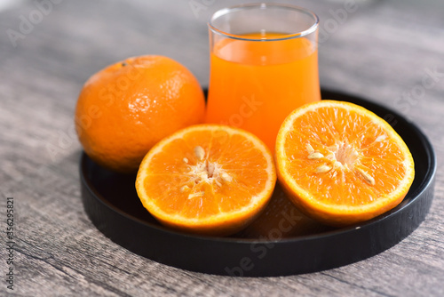 orange cut in half with the glass of orange juice on black tray