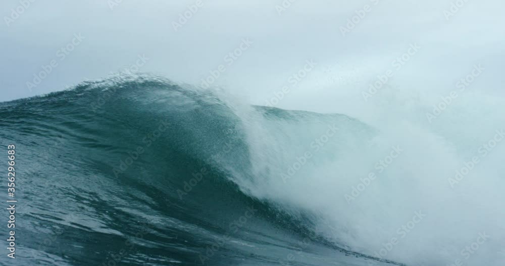 A large wave breaking into an arc into a dark blue sea with large plumes of spray. A large wave breaking into an arc into a dark blue sea with large plumes of spray.