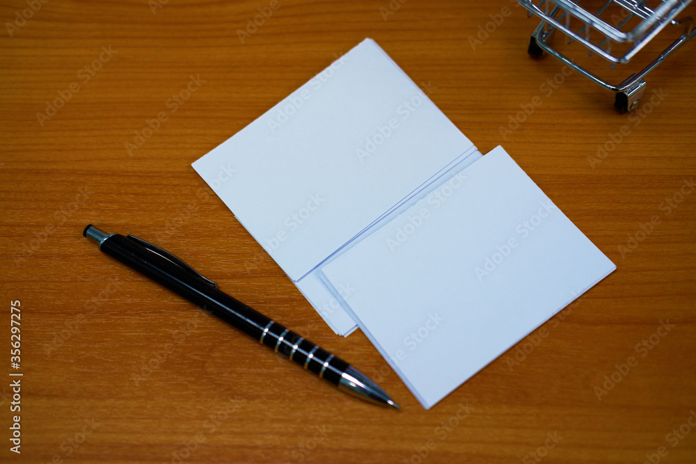 Stacked paper of blank white business cards simulated with an elegant black pen on the wooden table background. Stacked paper of blank white business cards simulated with an elegant black pen on the wooden table background.