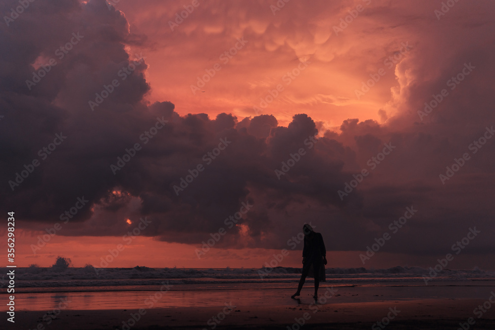 social distancing on the beach , pink and orange amazing cloudy sky , beautiful sunset , Bali Indonesia , solo outdoor walking 