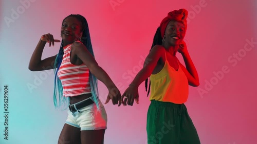 Two young black women dancing freely to a steady beat, in time, using the same moves.  