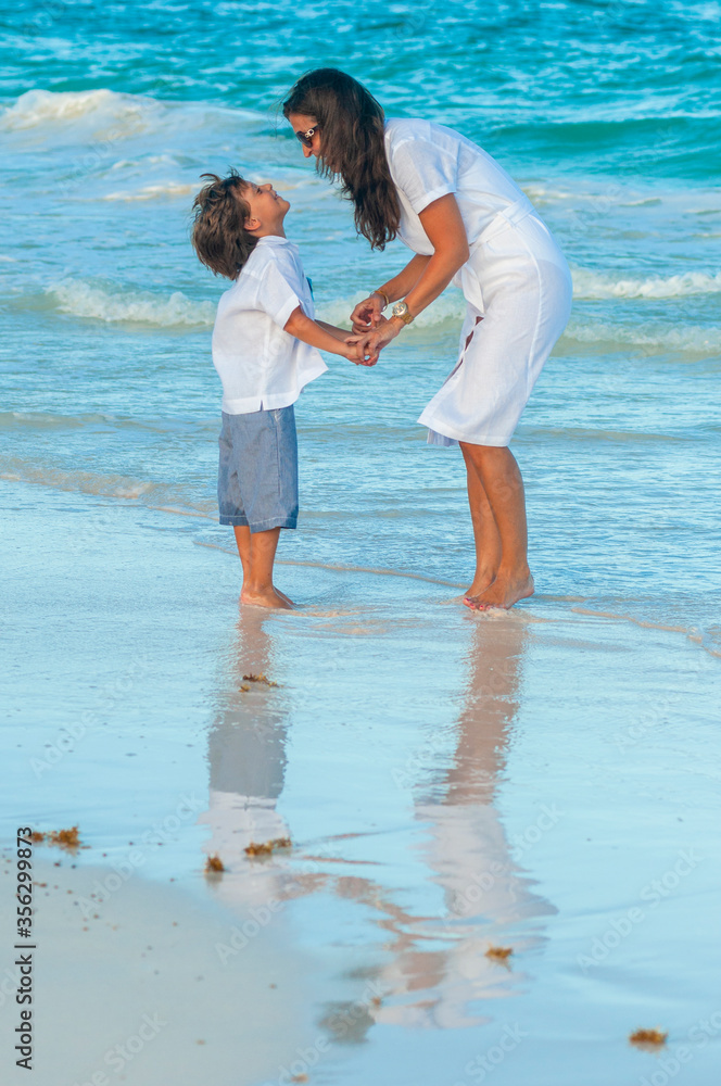 Mujer y niño con ropa de verano pasea juntos en playa del mar Caribe durante las vacaciones.