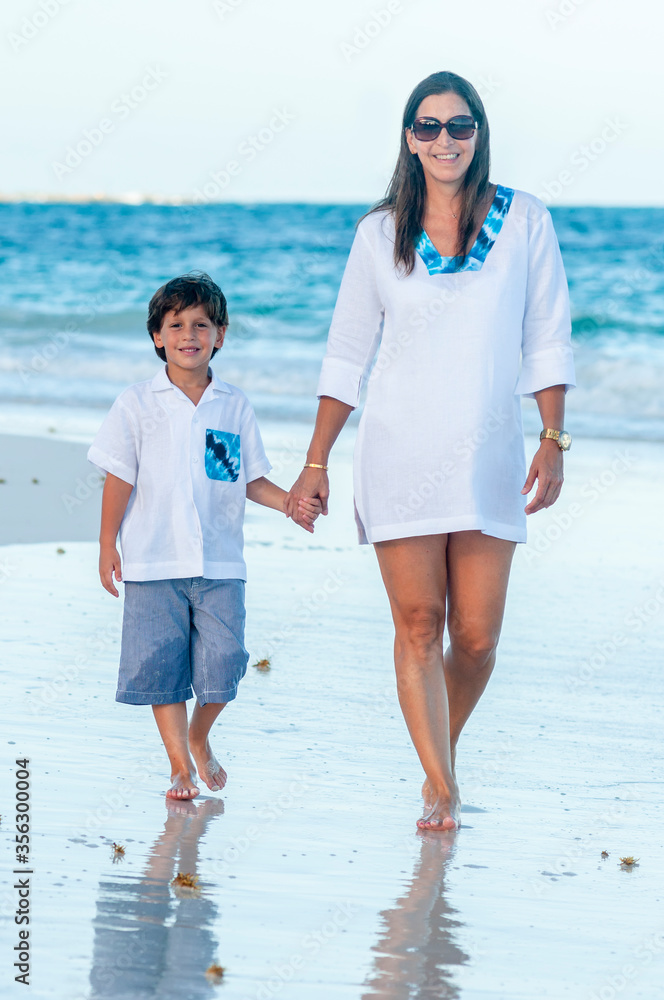 Foto de Mujer y niño con ropa de verano pasea juntos en playa del
