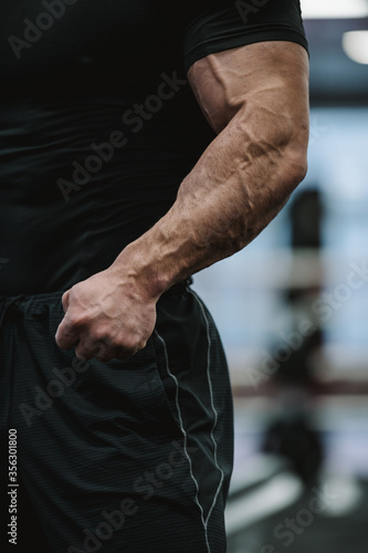 testosterone concept of body physique part of strong male in black sportswear showing strong arms with big vein during gym stress sport workout