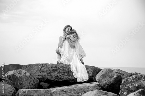 black and white photo, mother and daughter dancing on big rocks, on a wild beach near the sea