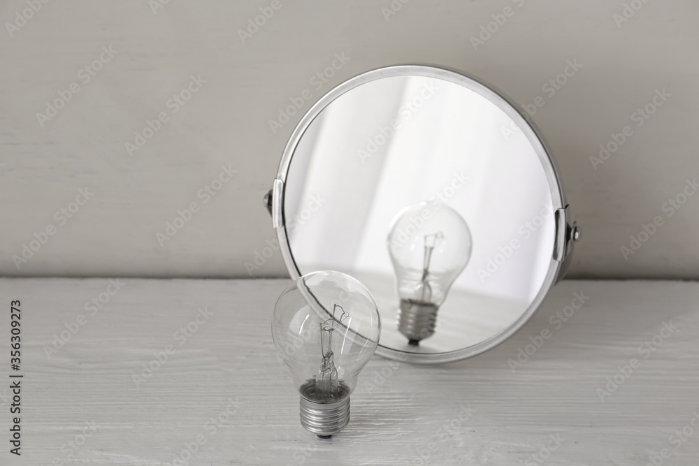 Light bulb near mirror on white wooden background