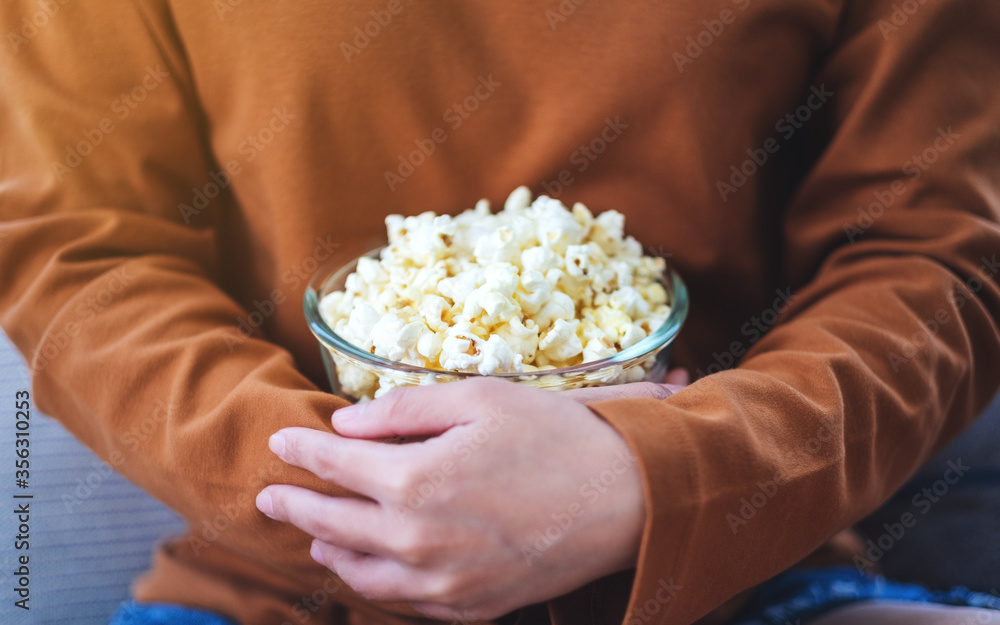 Close up image of a woman holding a bowl of pop corn while sitting on sofa at home Close up image of a woman holding a bowl of pop corn while sitting on sofa at home