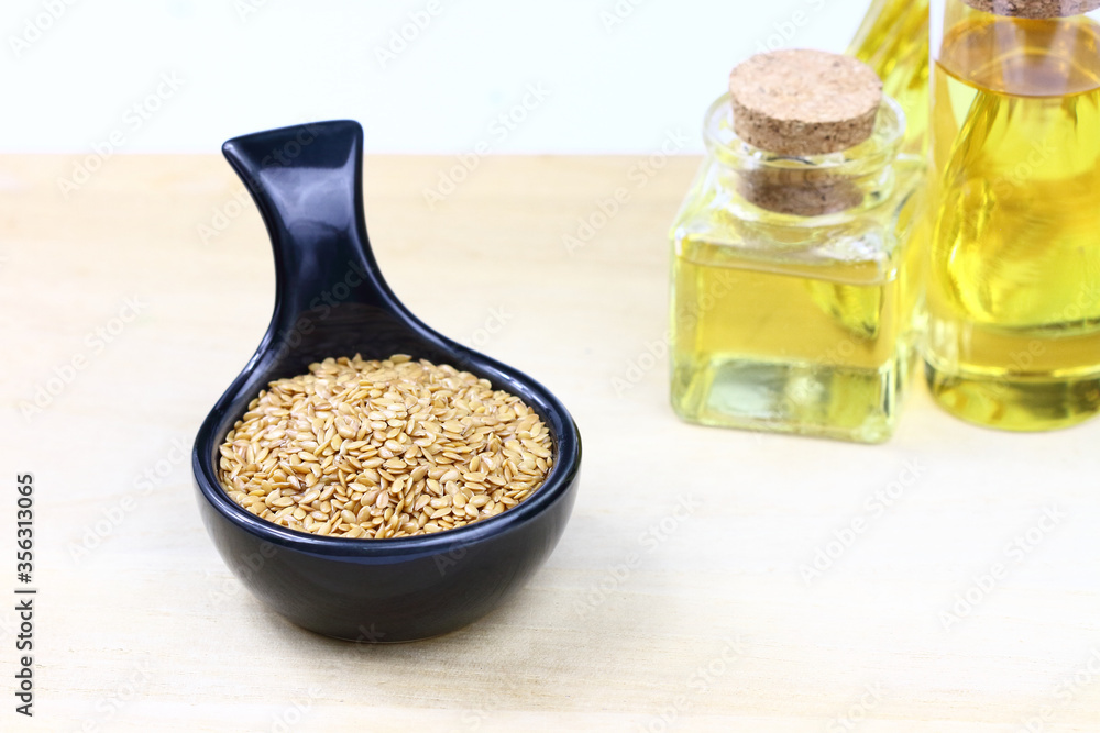 Flax seeds in a black ceramic bowl and flax seed oil in bottles on wooden board Flax seeds in a black ceramic bowl and flax seed oil in bottles on wooden board
