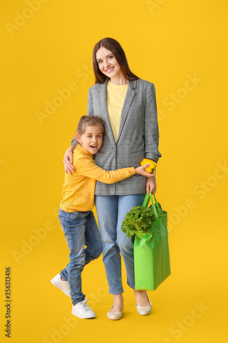 Mother and daughter with food in bag on color background