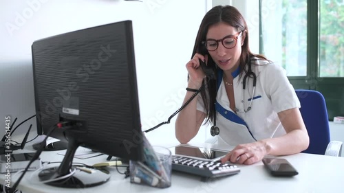 MS Female doctor using phone and digital tablet at desk in office / Vimercate, Monza and Brianza, Italy photo