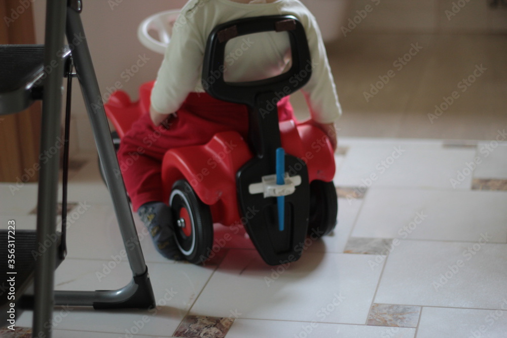 Fototapeta premium Small kid, child on a red car toy. Driving in the room alone.