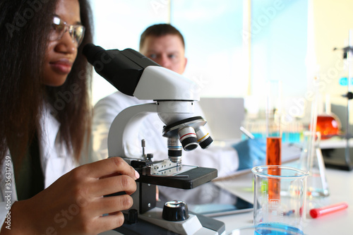 Two scientists of a student chemist are conducting research using microscope for bacterial contamination of water to search for vaccine to treat diseases in medicine