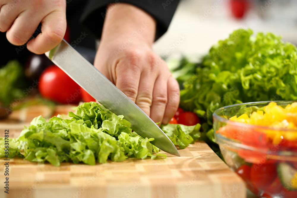 Cook holds knife in hand and cuts on cutting board green for salad or fresh vegetable soup with vitamins. Raw food and vegetarian recipe book in modern society popular concept.