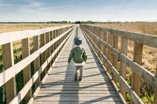 Boy walking long way in nature. Child exploring the world landscape. Parenthood and childhood background. Travel with small cute son. View from behind.