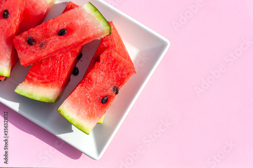 Summer creative watermelon layout. Sweet red slices of  ripe watermelon on white plate on pink background. Healthy food summertime concept. Intarnational watermelon day.Copy space photo