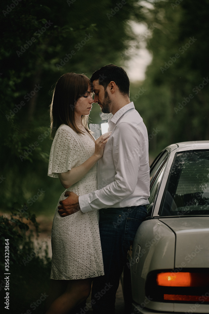 A guy and a girl are hugging next to a car. Romantic date evening walk. The relationship between people is love and tenderness. A guy and a girl are hugging next to a car. Romantic date evening walk. The relationship between people is love and tenderness.