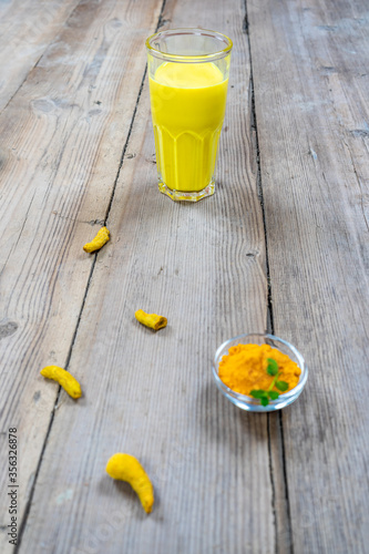 Golden milk in a glass cup on a wooden background