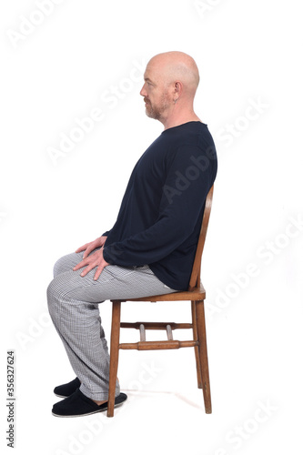 man in pajamas sitting o a chair on white background, side view
