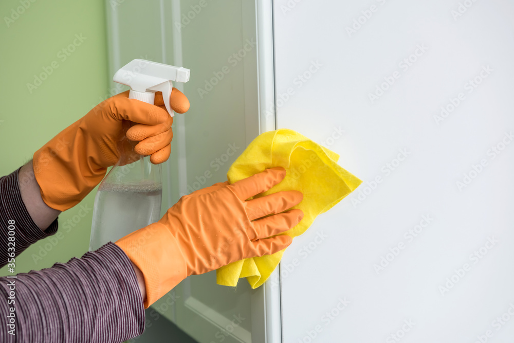 Male's hands in yellow rag glove with spray and sponge washing  kitchen wooden furniture