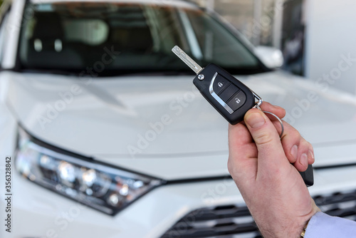 Male hand with car keys against new car in showroom