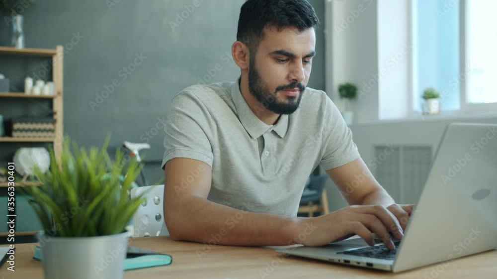 Smiling Arabian man is using laptop texting enjoying friendly communication at home at table. Modern technology, internet and people concept. Smiling Arabian man is using laptop texting enjoying friendly communication at home at table. Modern technology, internet and people concept.