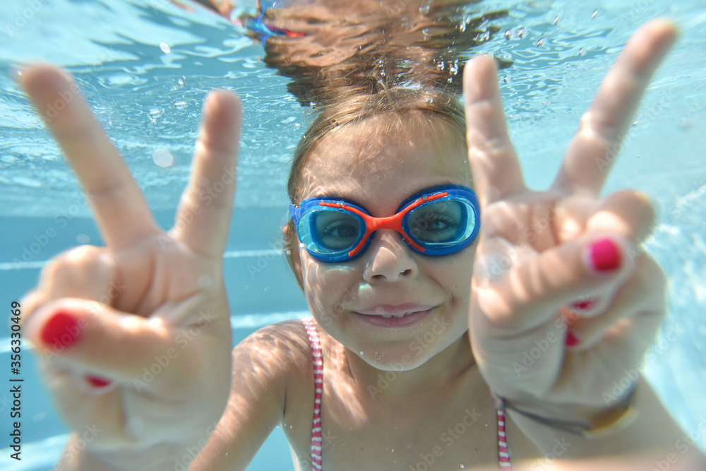 Portrait of cute girl with goggles swimming under pool water