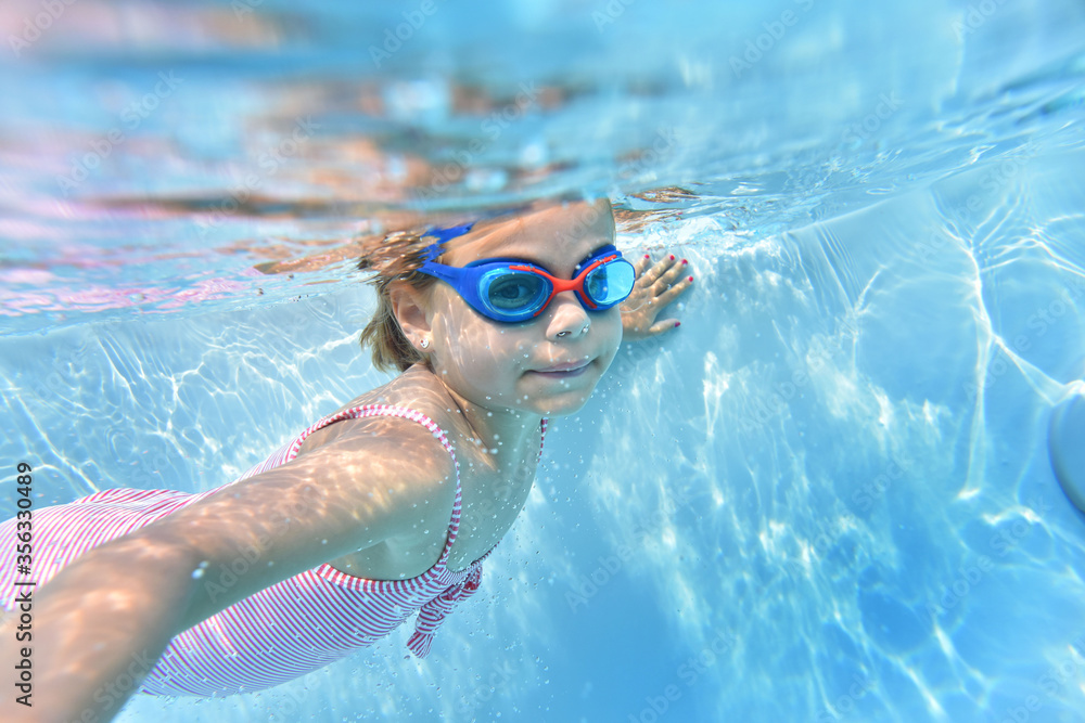 Naklejka premium Portrait of cute girl with goggles swimming under pool water