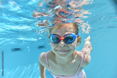 Portrait of cute girl with goggles swimming under pool water © goodluz